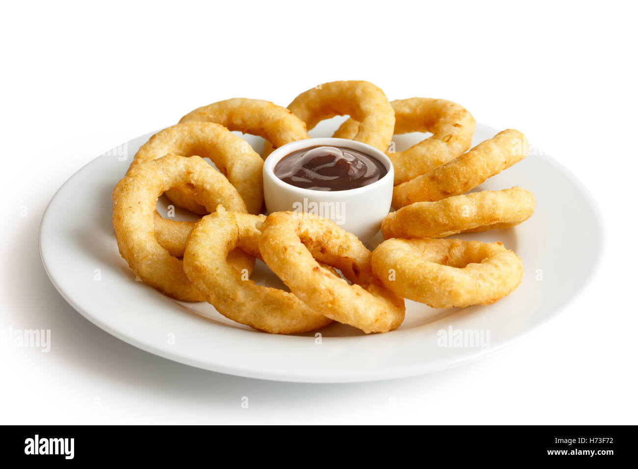 Heap of deep fried onion or calamari rings with barbecue dip on white plate. Stock Photo