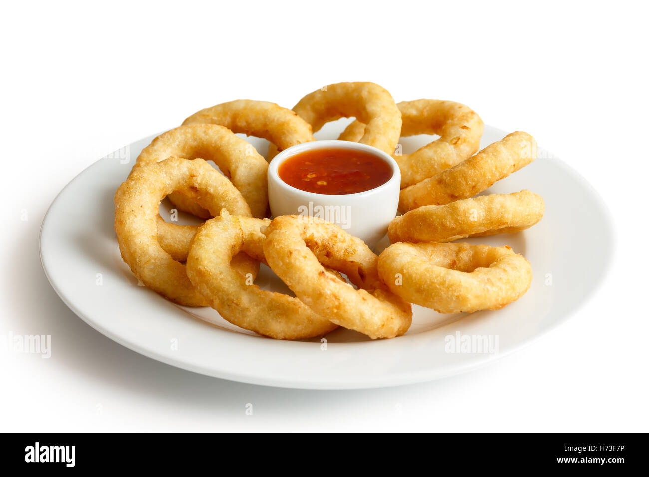 Heap of deep fried onion or calamari rings with chilli dip on white plate. Stock Photo