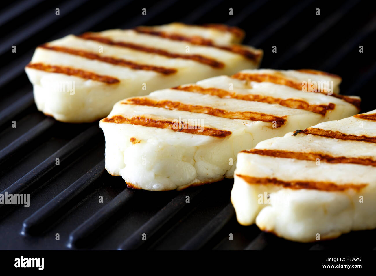 Three grilled slices of halloumi cheese on grill in perspective. With grill marks. Stock Photo