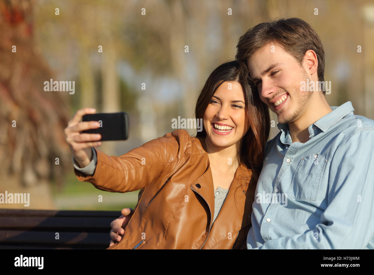 Couple taking selfie photo sitting in a bench Stock Photo