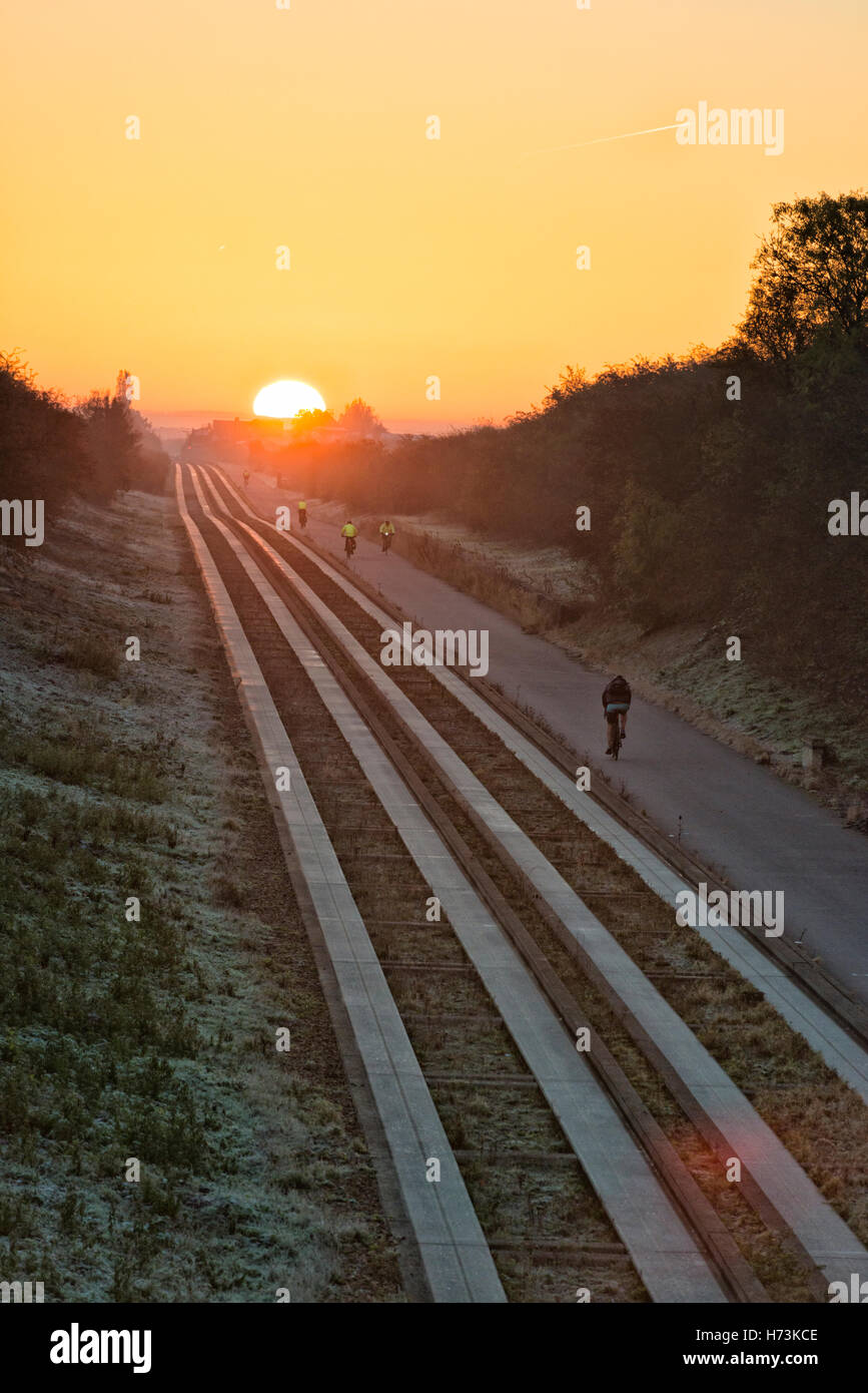 Over, Cambridgeshire UK, 2nd November 2016.  Cyclists ride towards Cambridge as the sun rises over the tracks on a clear, crisp, frosty autumn morning. The clear air and first frost of this autumn in the East of the UK shed a golden glow on the morning commute. Credit Julian Eales/Alamy Live News Stock Photo