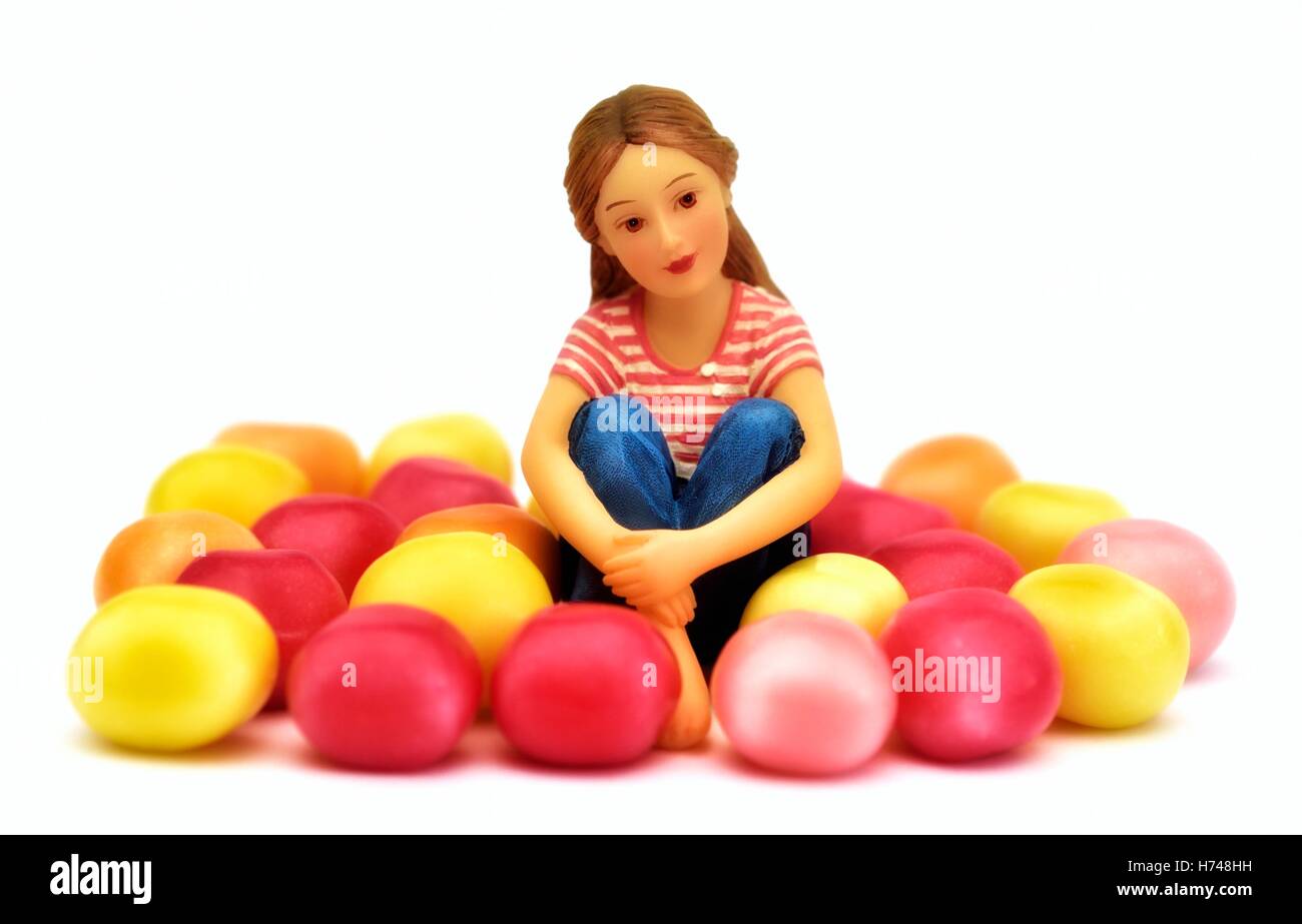 A figurine teenage girl sitting amongst some candy sweets on a white background. Stock Photo