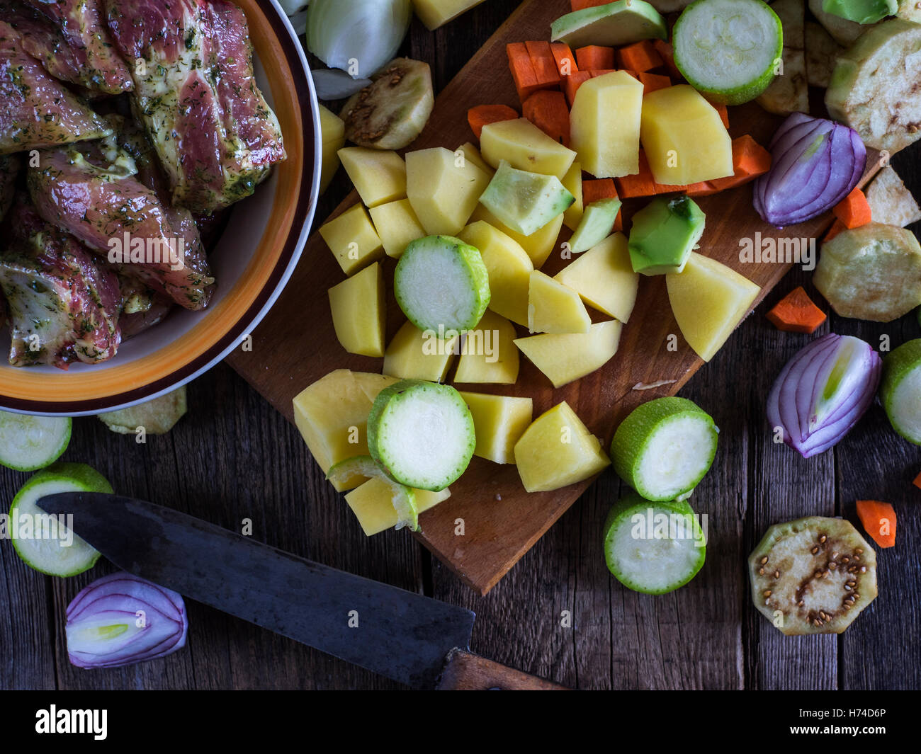 Marinated raw ribs and chopped vegetables on a cutting board on an old weathered wooden table Stock Photo