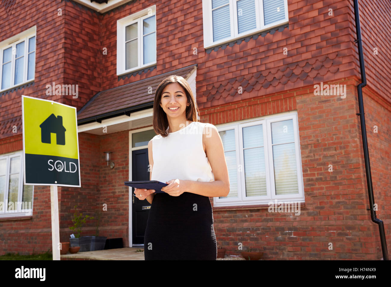 Female Realtor Standing Outside Residential Property Stock Photo