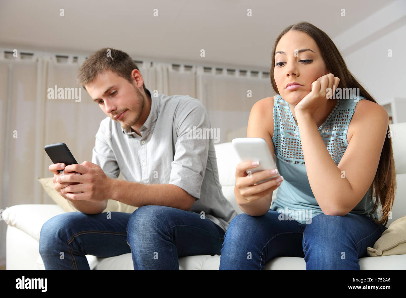Bored couple online with their smart phones sitting on a couch in the living room at home Stock Photo
