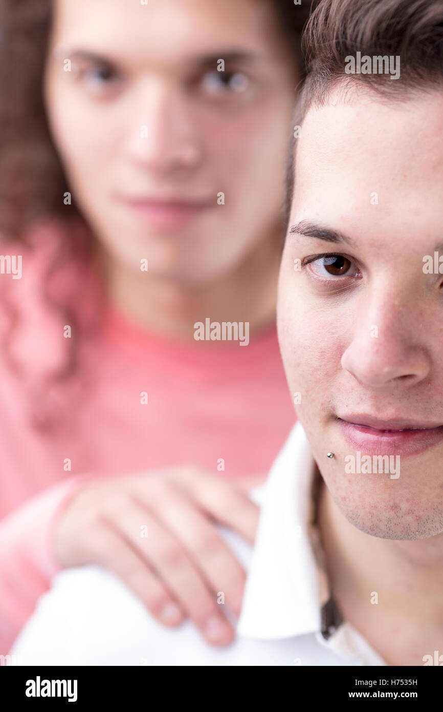 portrait of young short-haired gay man looking at you while his boyfriend supports him blurred on the background Stock Photo