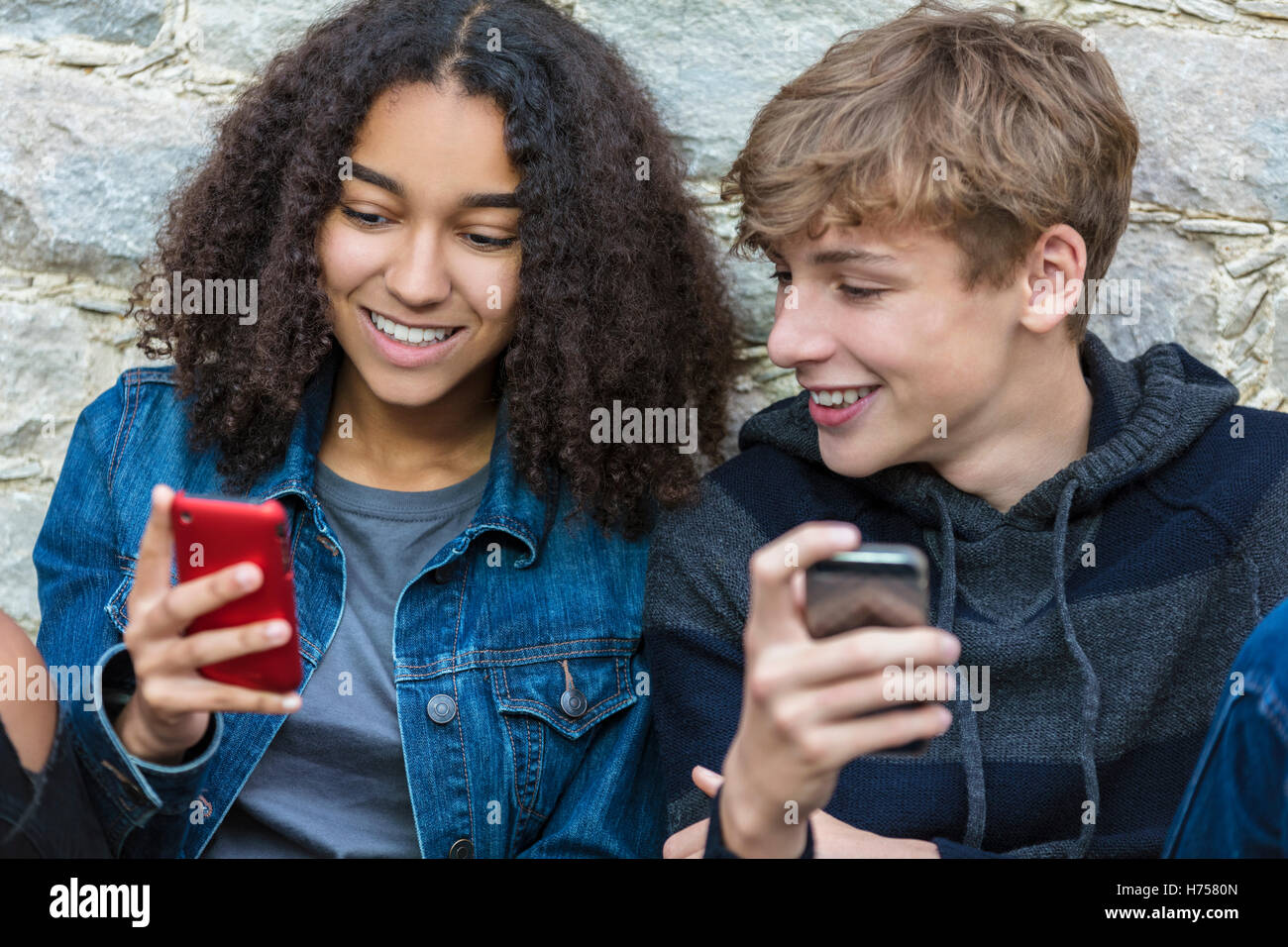 Mixed race African American girl, interracial teenagers boy and girl, male and female, texting and using mobile cell phone Stock Photo