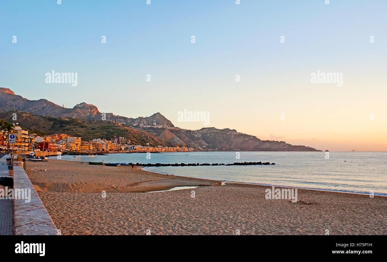 The romantic sunrise over the central beach of Giardini Naxos with the view on the sharp rocks of Taormina, Sicily, Italy. Stock Photo
