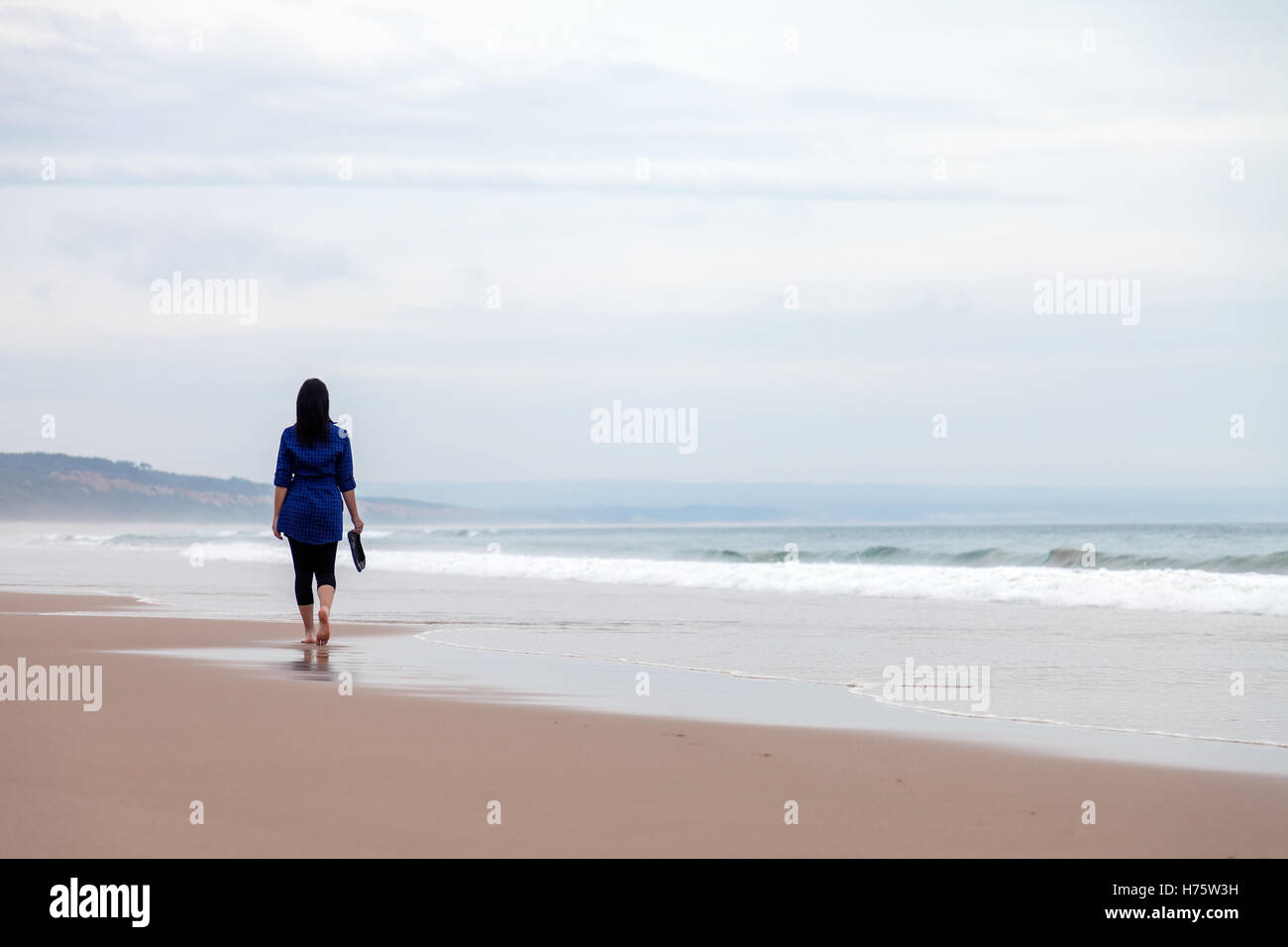 Young woman walking away alone in a deserted beach on an Autumn day. Stock Photo