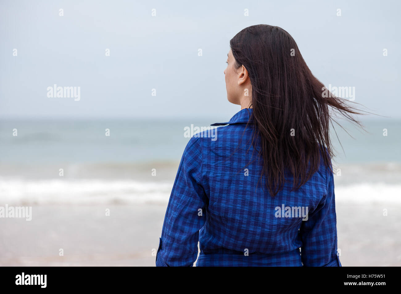 Lonely and depressed woman standing in front of the sea in a deserted beach on an Autumn day. Stock Photo