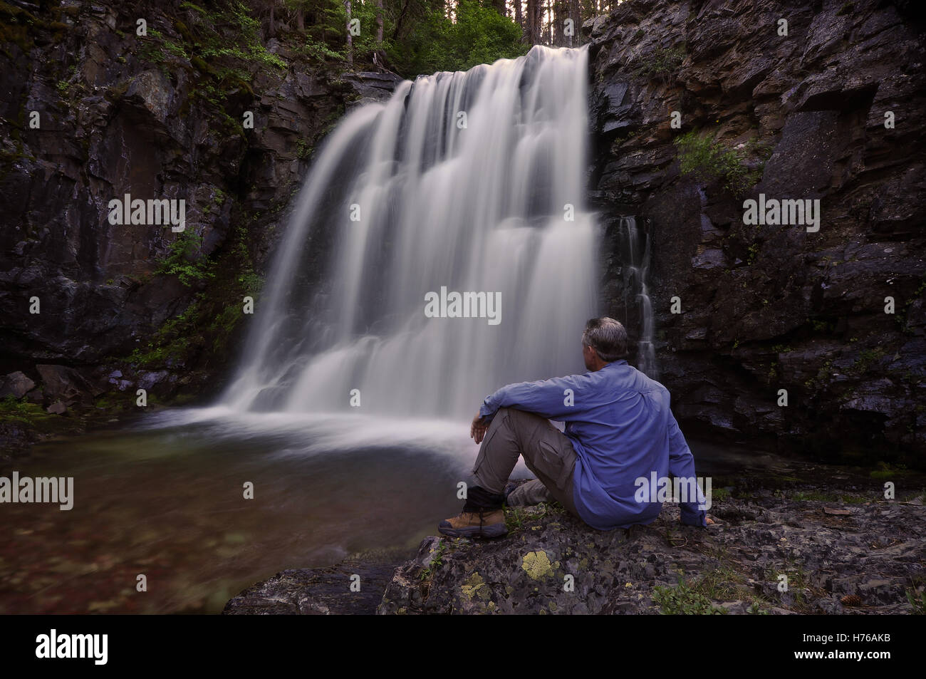 Man sitting by Rockwell Falls, Glacier National Park, Montana, United States Stock Photo