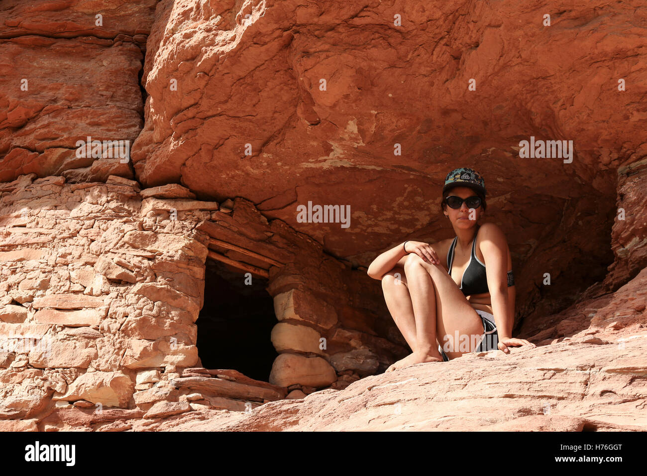 An athletic young woman sits next to a small cliff dwelling on the Green River, in Canyonlands National Park Stock Photo