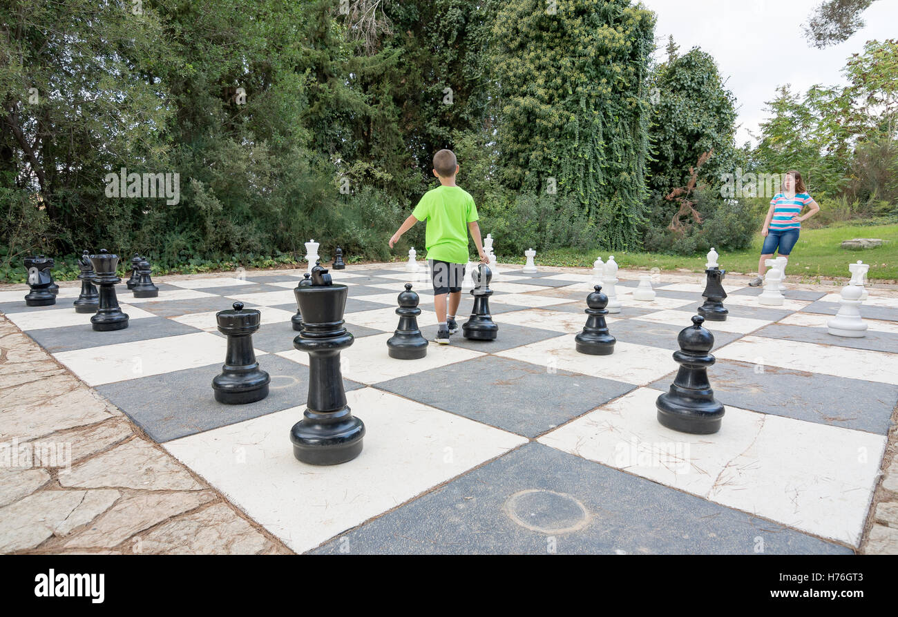 Brother and sister siblings playing a game of giant outdoor chess with ...