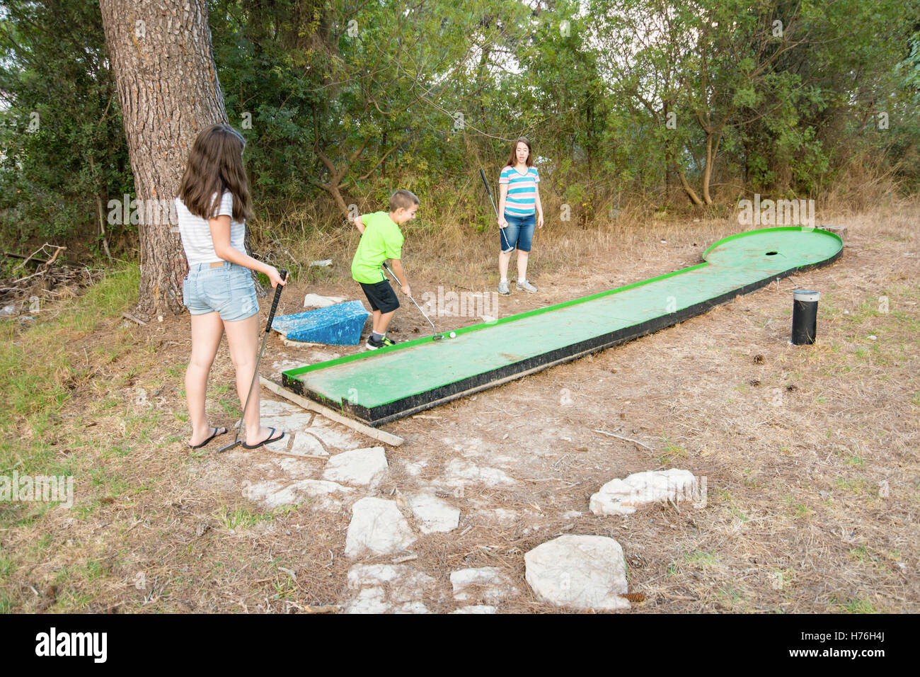 Three siblings playing outdoor miniature golf in a Galilee forest in the north of Israel Stock Photo