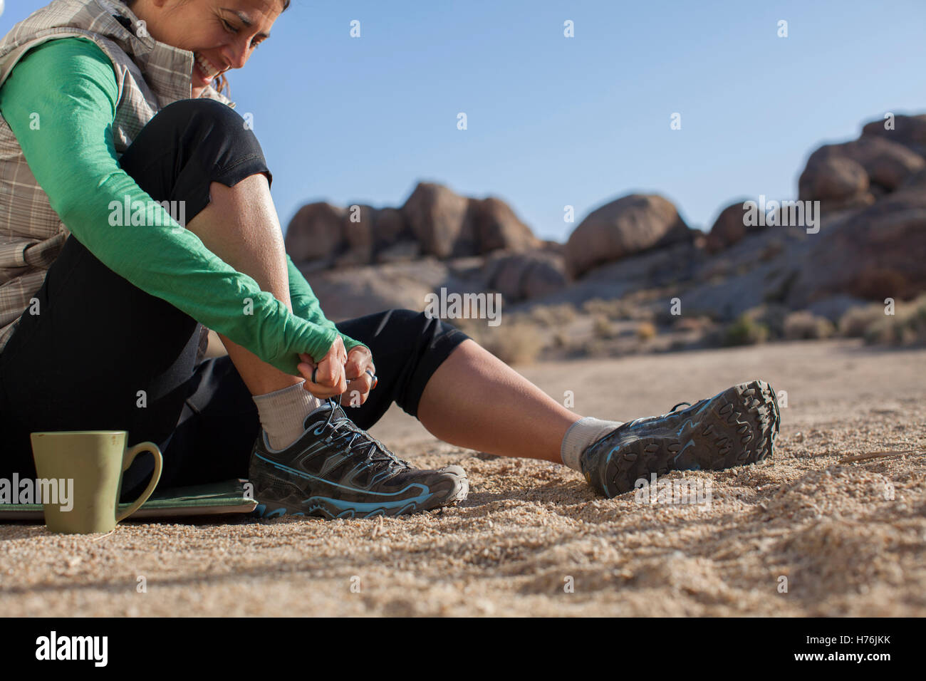 Cropped image of an adult woman in camp with her coffee putting on shoe to go for a trail run. Stock Photo