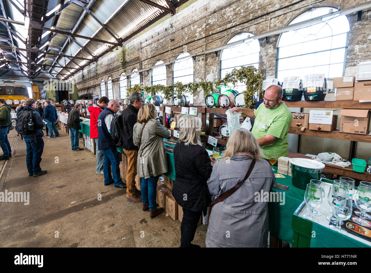 CAMRA beer festival in old locomotive shed at Tunbridge Wells, UK. People selecting beers from various casks, beer barrels, behind a long counter. Stock Photo