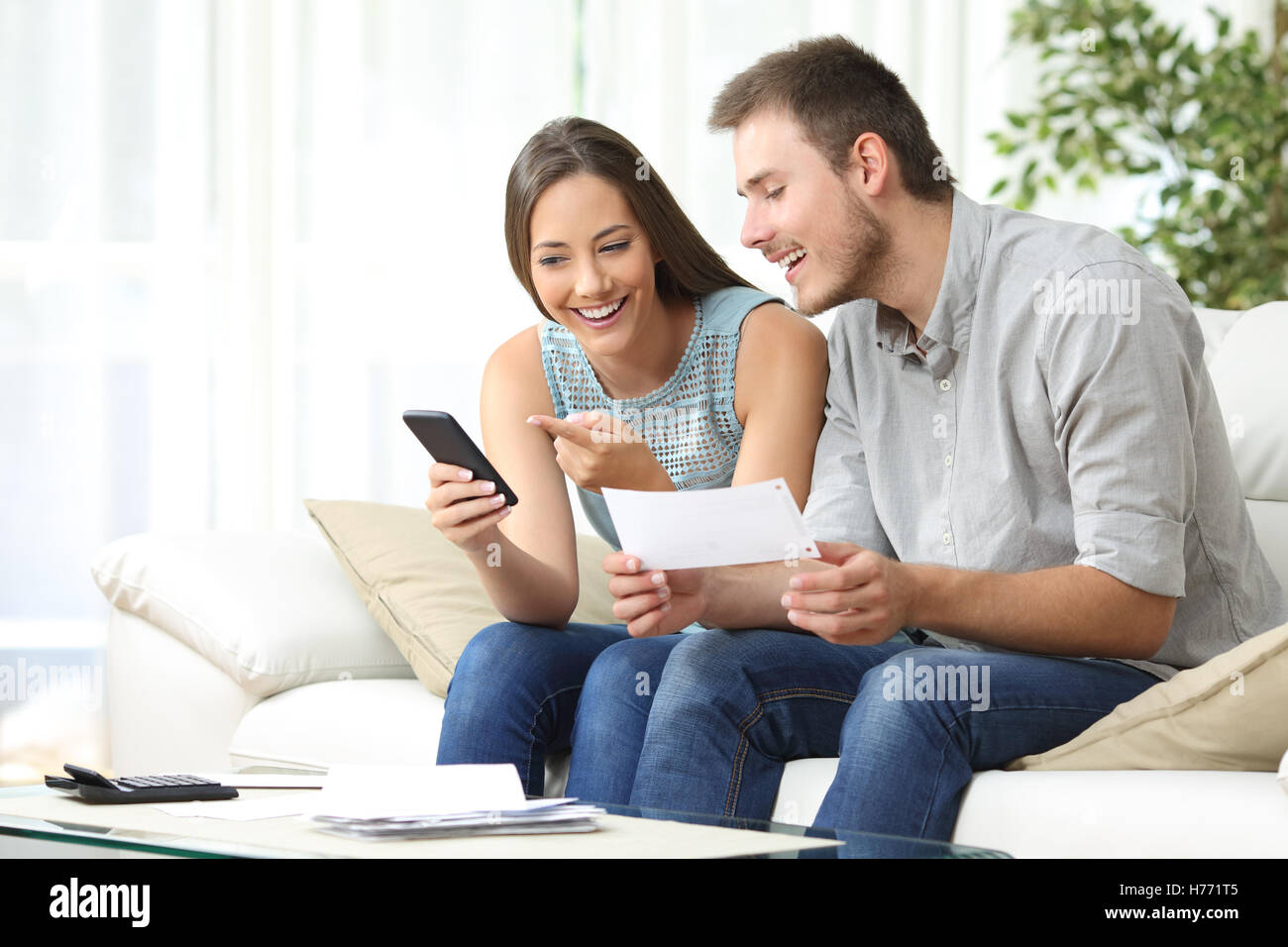 Couple doing accounting on line with a phone bank app sitting on a couch in the living room at home Stock Photo