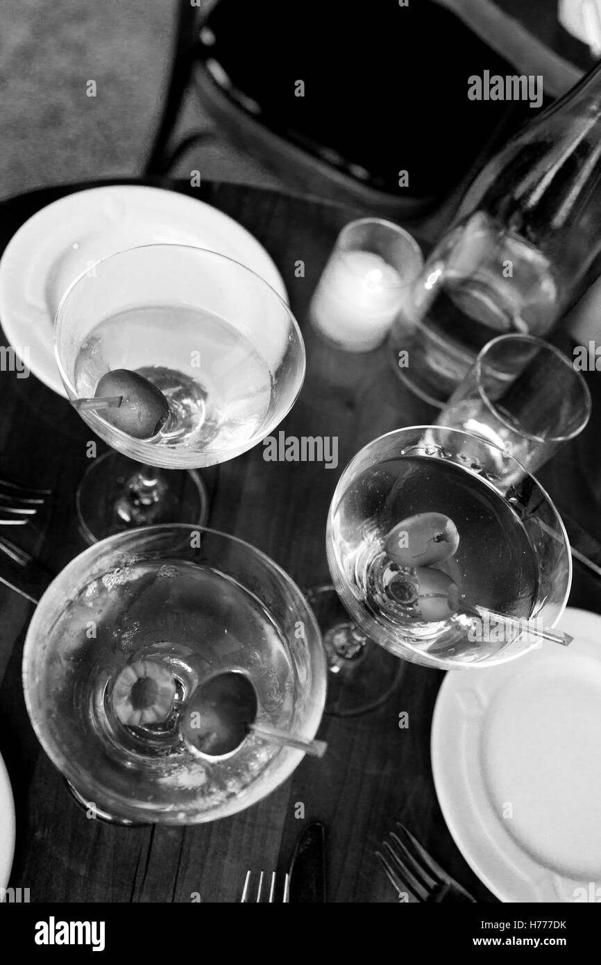 Three Vodka, or Gin Martinis in classic glasses with olives.  Photographed in a vertical format from overhead in a cafe.  No people, no food.  Wating Stock Photo