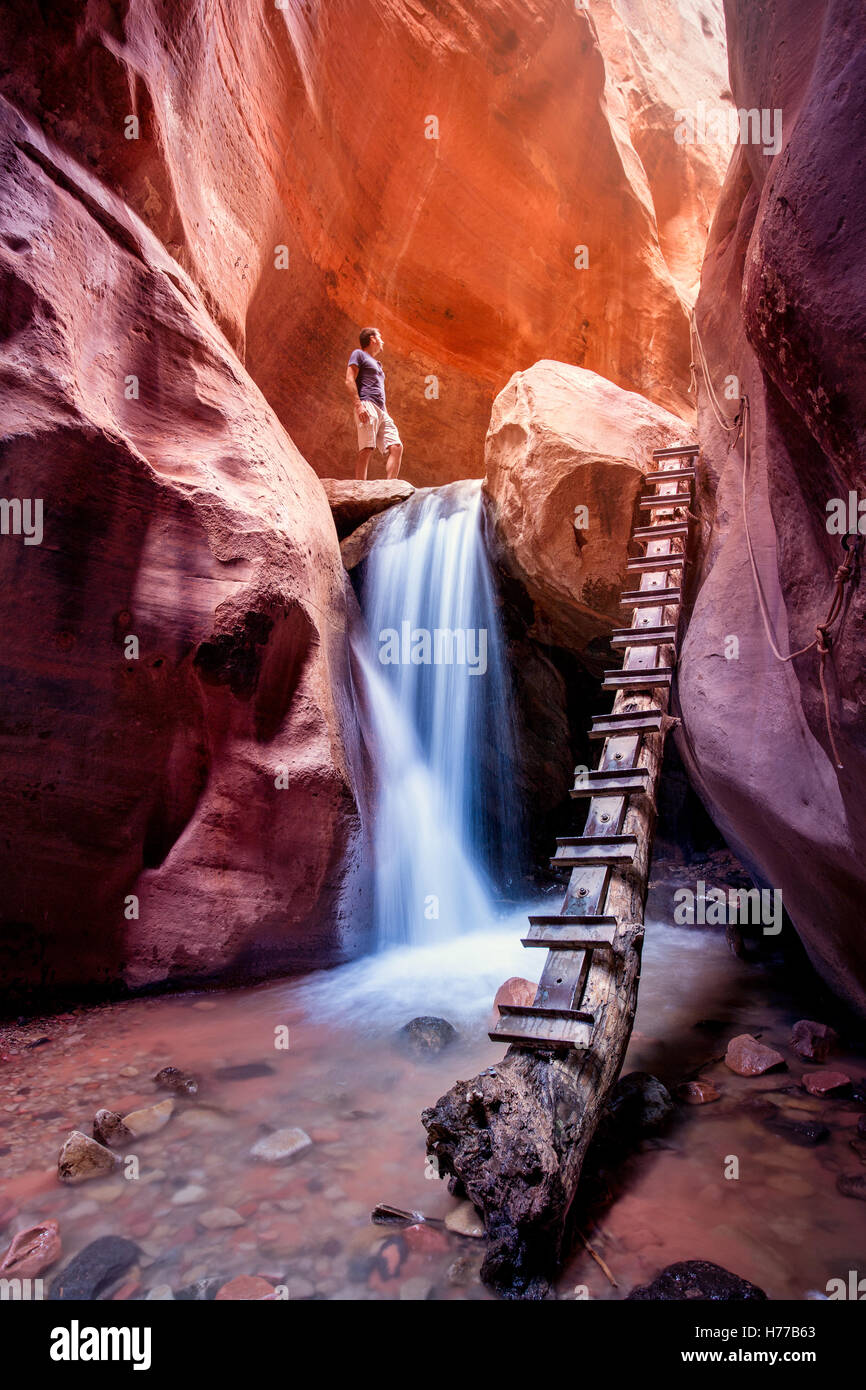 Woman standing above waterfall, red slot canyon, Utah, United States Stock Photo