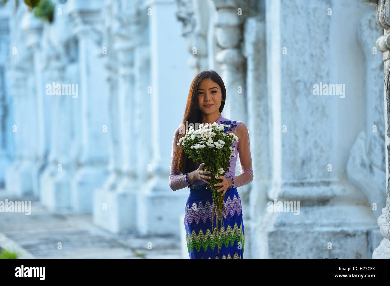 Young woman holding flowers outside temple, Mandalay, Myanmar Stock Photo