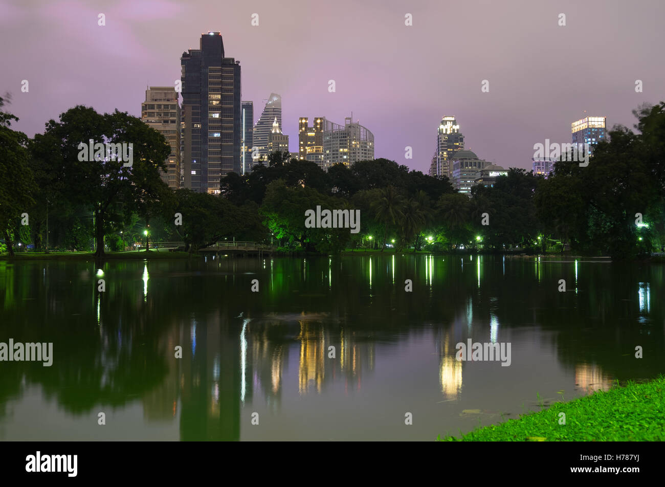 Urban city, tall buildings reflection and lights at rainy sunset day in lake in Lumphini Park Bangkok. Stock Photo