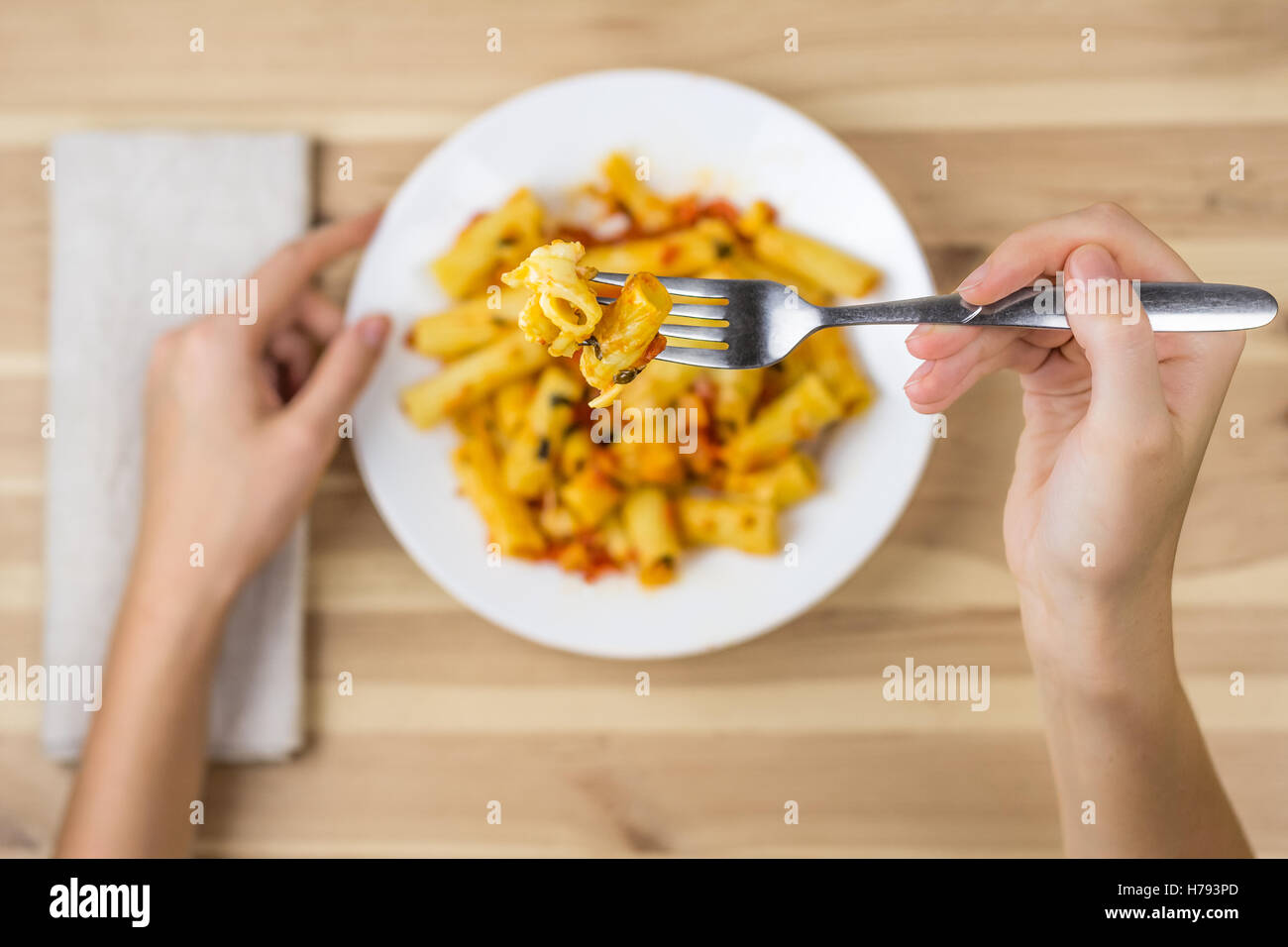 Cooked tortiglioni pasta on fork close up. Female hand holding fork above the plate of baked