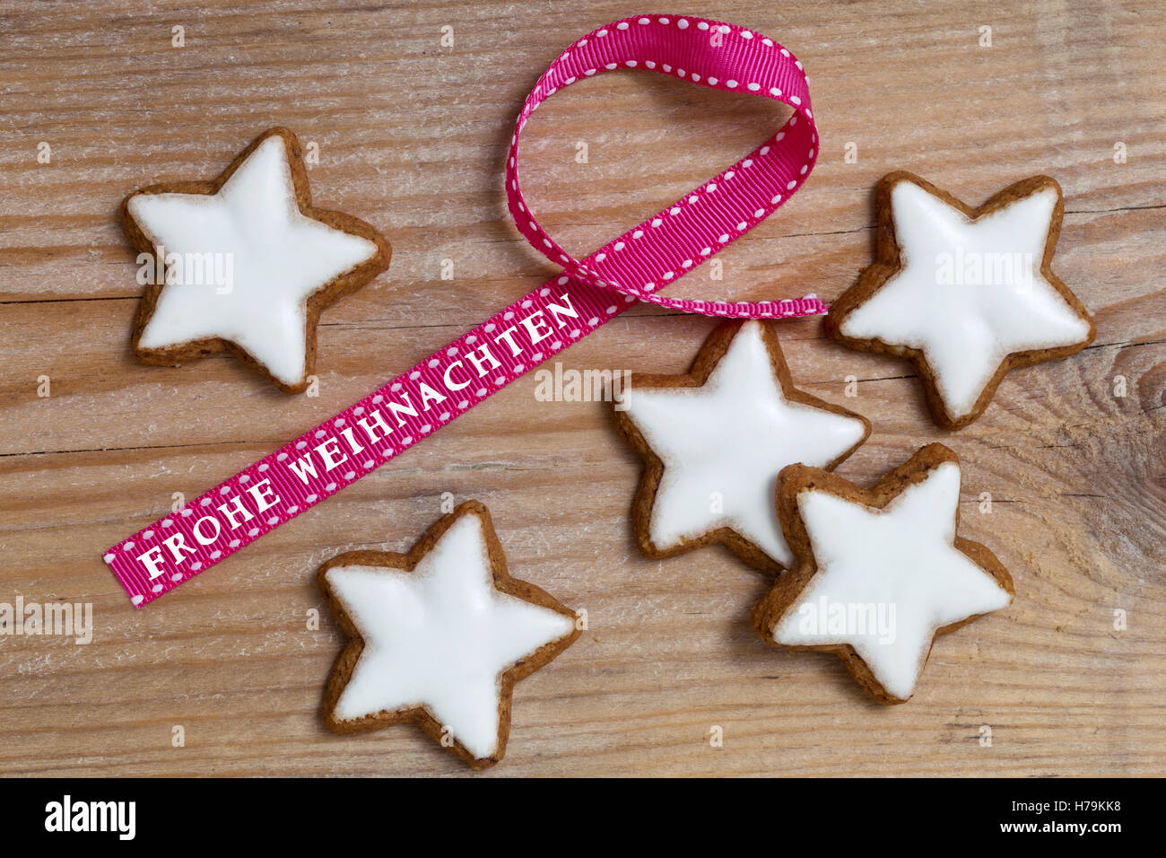 Cinnamon star on wood with Frohe Weihnachten (in german merry christmas) gift ribbon. Stock Photo