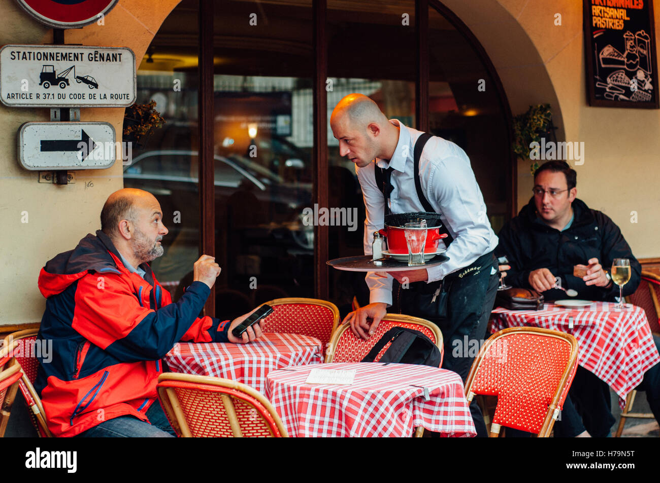 PARIS, FRANCE - NOVEMBER 4, 2015: Man talks with waiter at street cafe on November 4, 2015 in Montmartre. Waiter holds tray with Stock Photo
