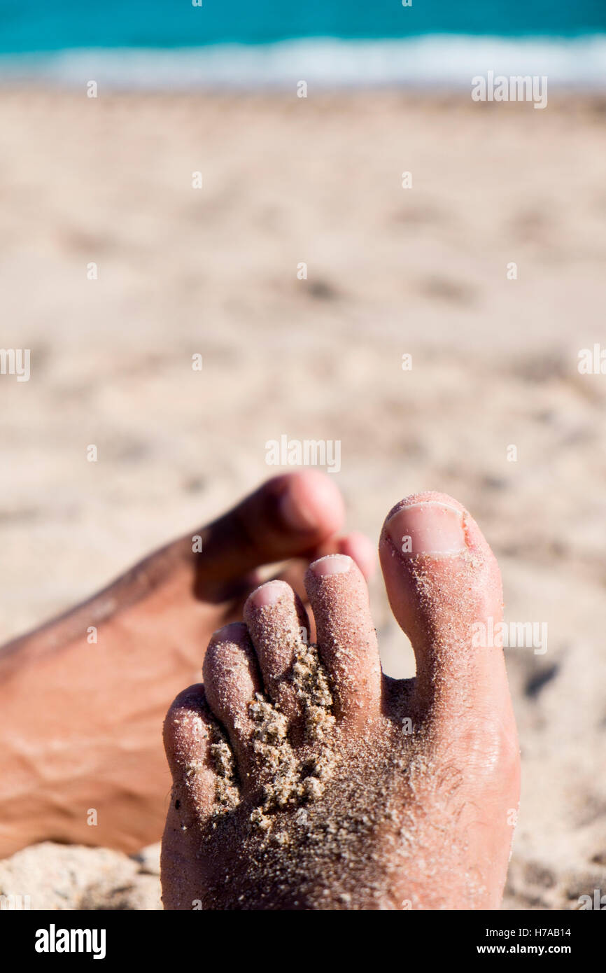 closeup of the feet of two young men playing footsie on the beach Stock Photo