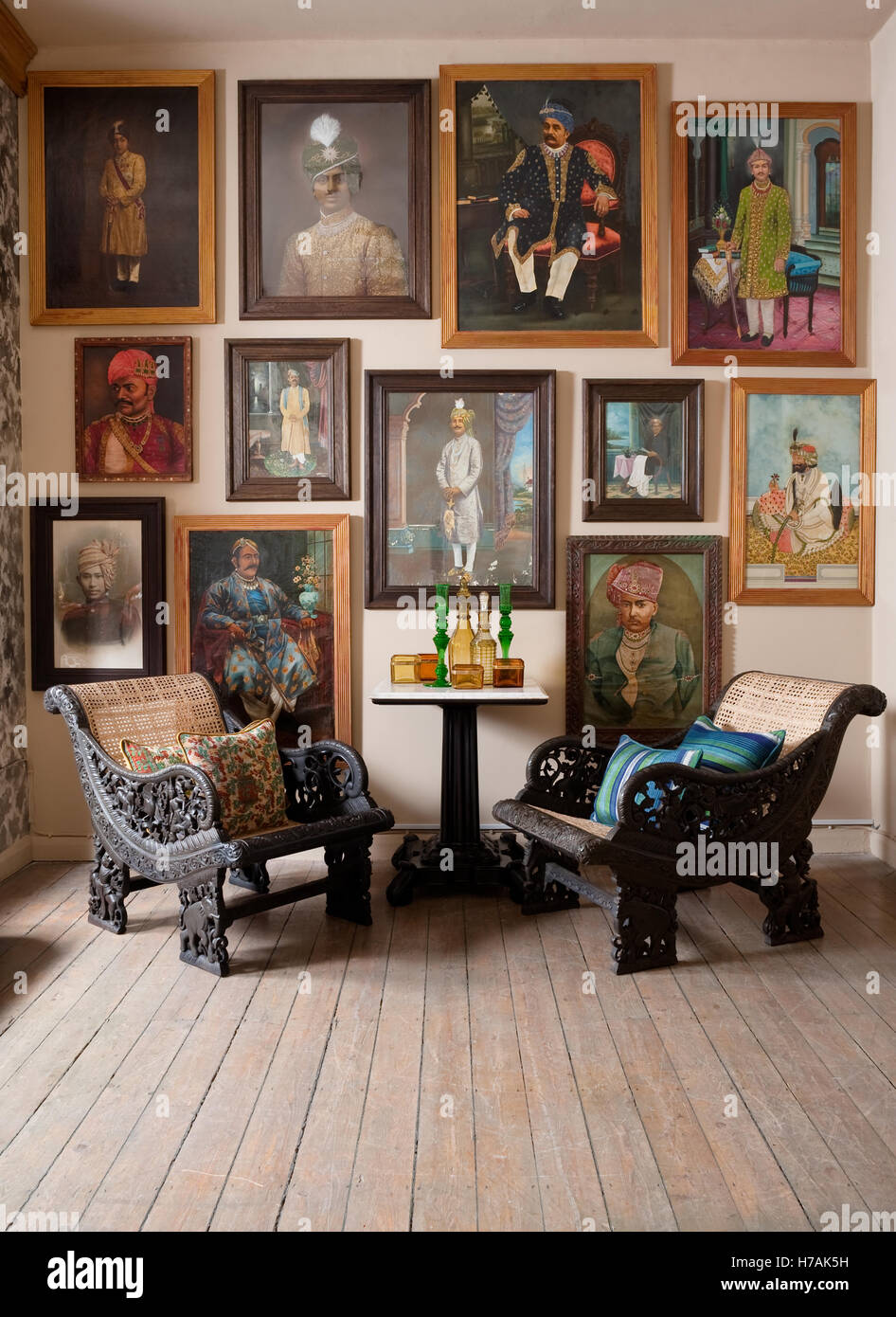 Ornately carved wood Indo-portugese caned easy chairs in room with wooden flooring and Indian maharaja portraits Guinevere's Stock Photo