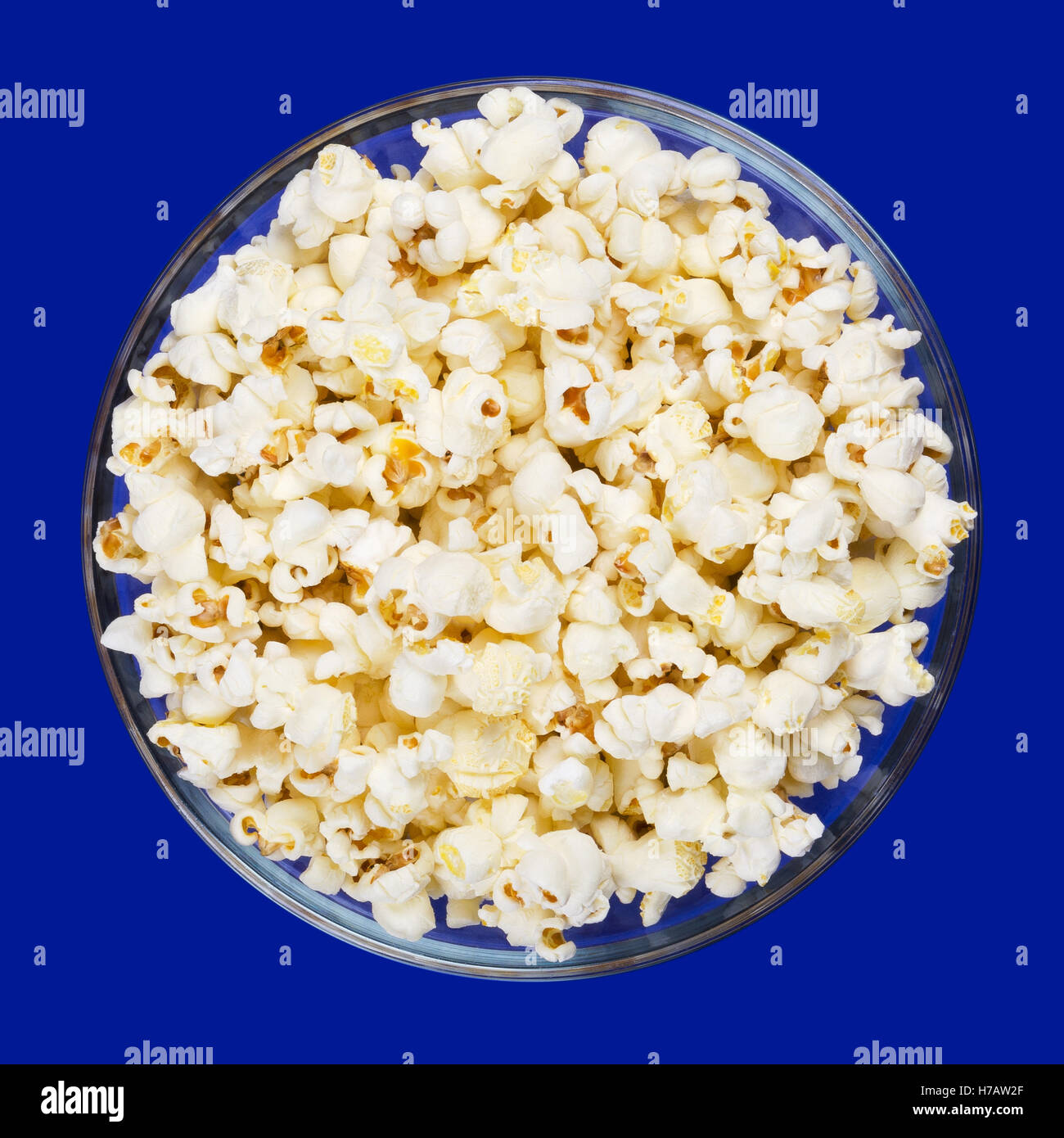 Popcorn in glass bowl on blue background. Butterfly shaped popped