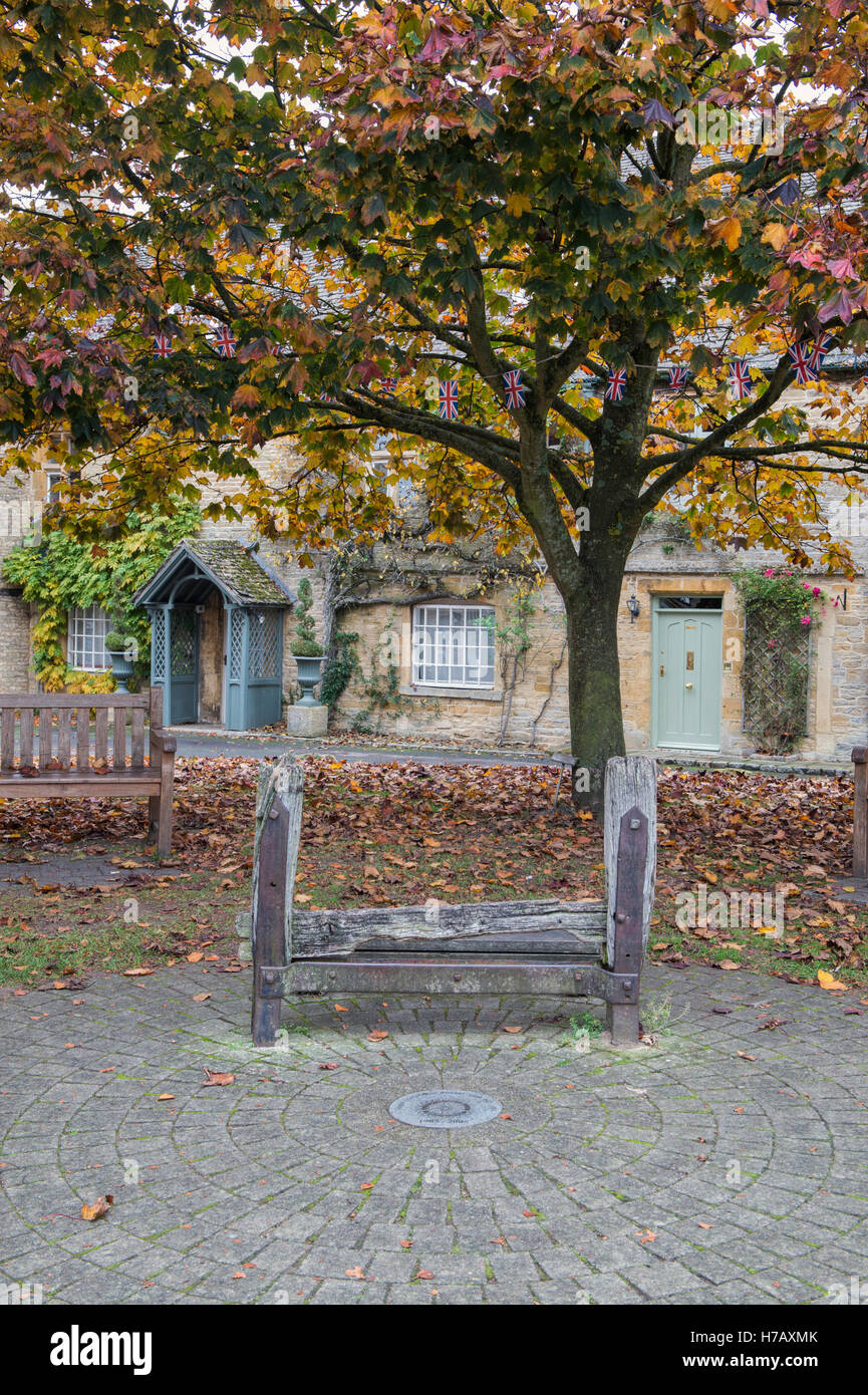 Old penal stocks in front of cottages in autumn. Stow on the Wold, Gloucestershire, England Stock Photo