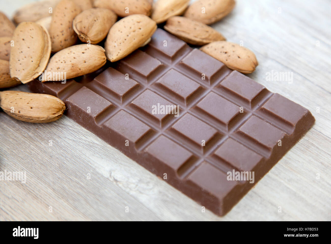 Close up of a bunch of raw almonds in their shells on a bar of milk chocolate on wooden background Stock Photo