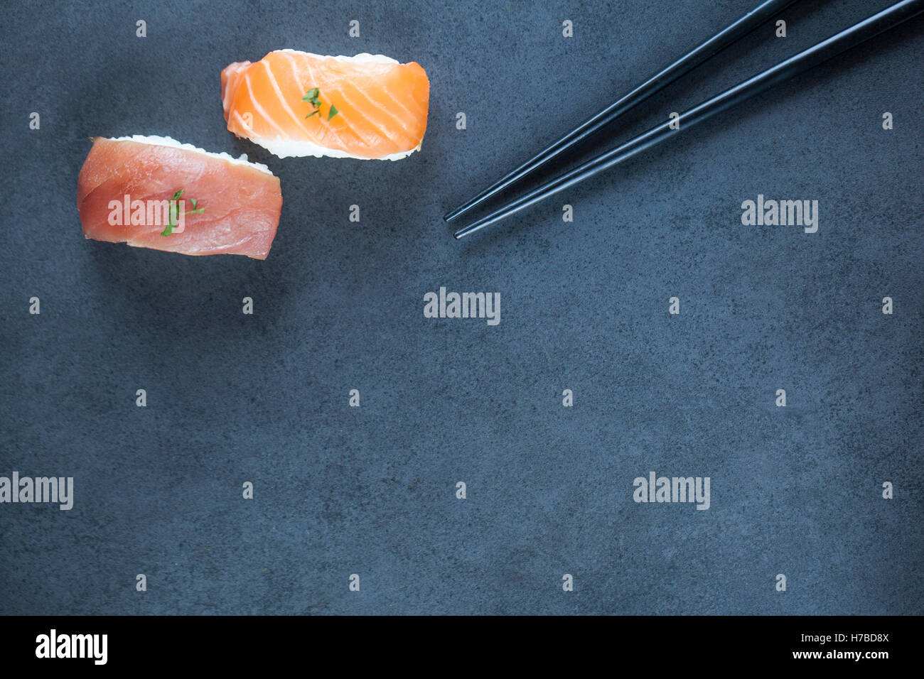 Close-up view of fresh tuna and salmon nigiri and chopsticks on a dark plate with copy space. Stock Photo