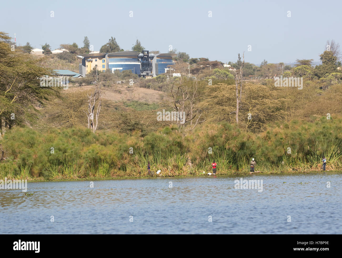 African fishermen at lake edge with KENGEN building behind Lake Naivasha Kenya Stock Photo