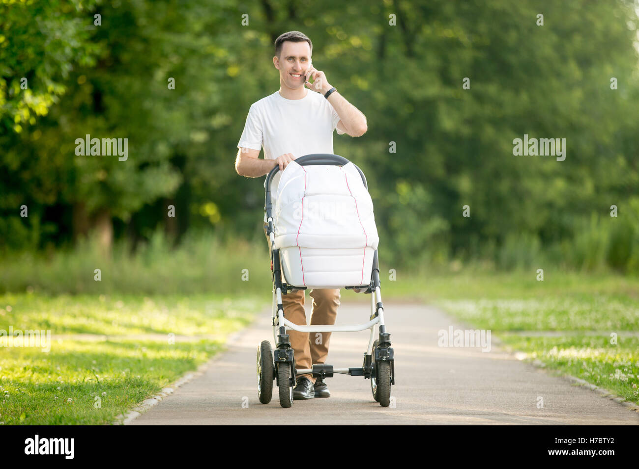 Man pushing pram and talking on phone in park Stock Photo