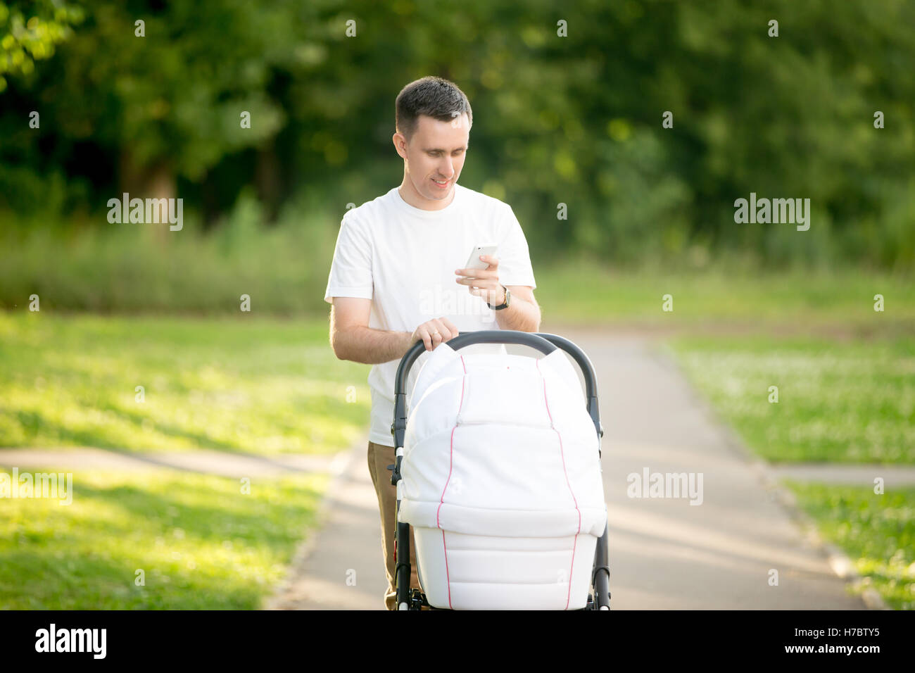 Man with baby carriage in park looking at phone screen Stock Photo