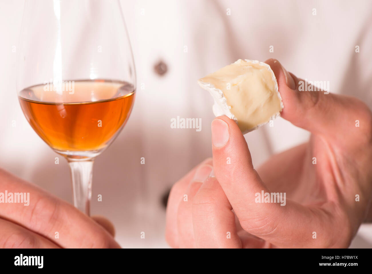 Sherry in a glass and hand holding a piece of brie cheese. Snack or appetizer. Stock Photo