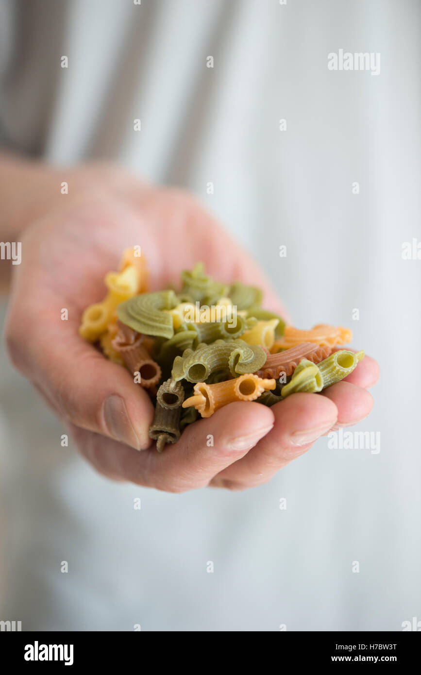 Colorful pasta in close up. Hand of chef holding uncooked macaroni in different colors. Stock Photo