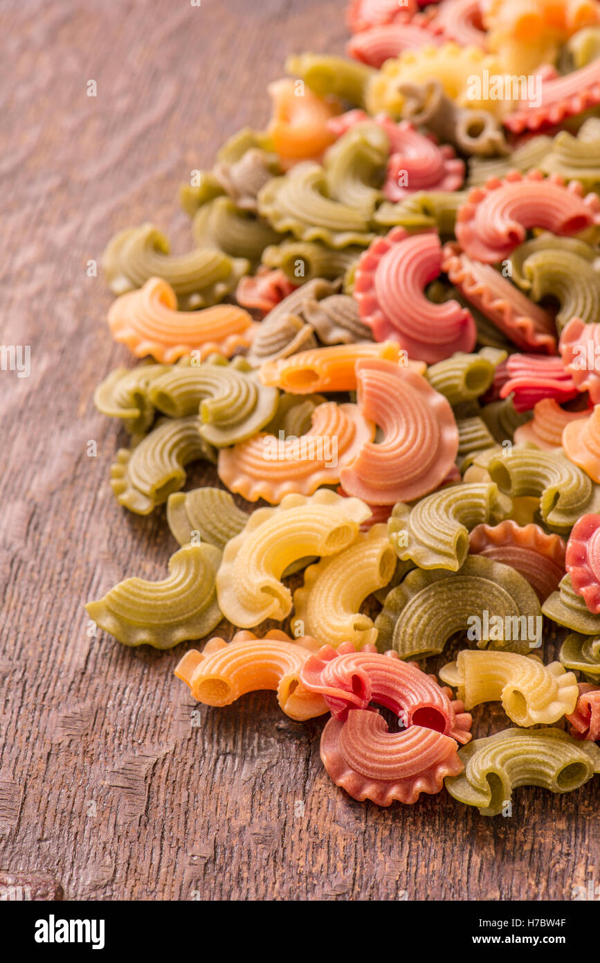 Colorful pasta in close up. Macaroni in different colors on rustic wooden table. Traditional italian cuisine. Stock Photo
