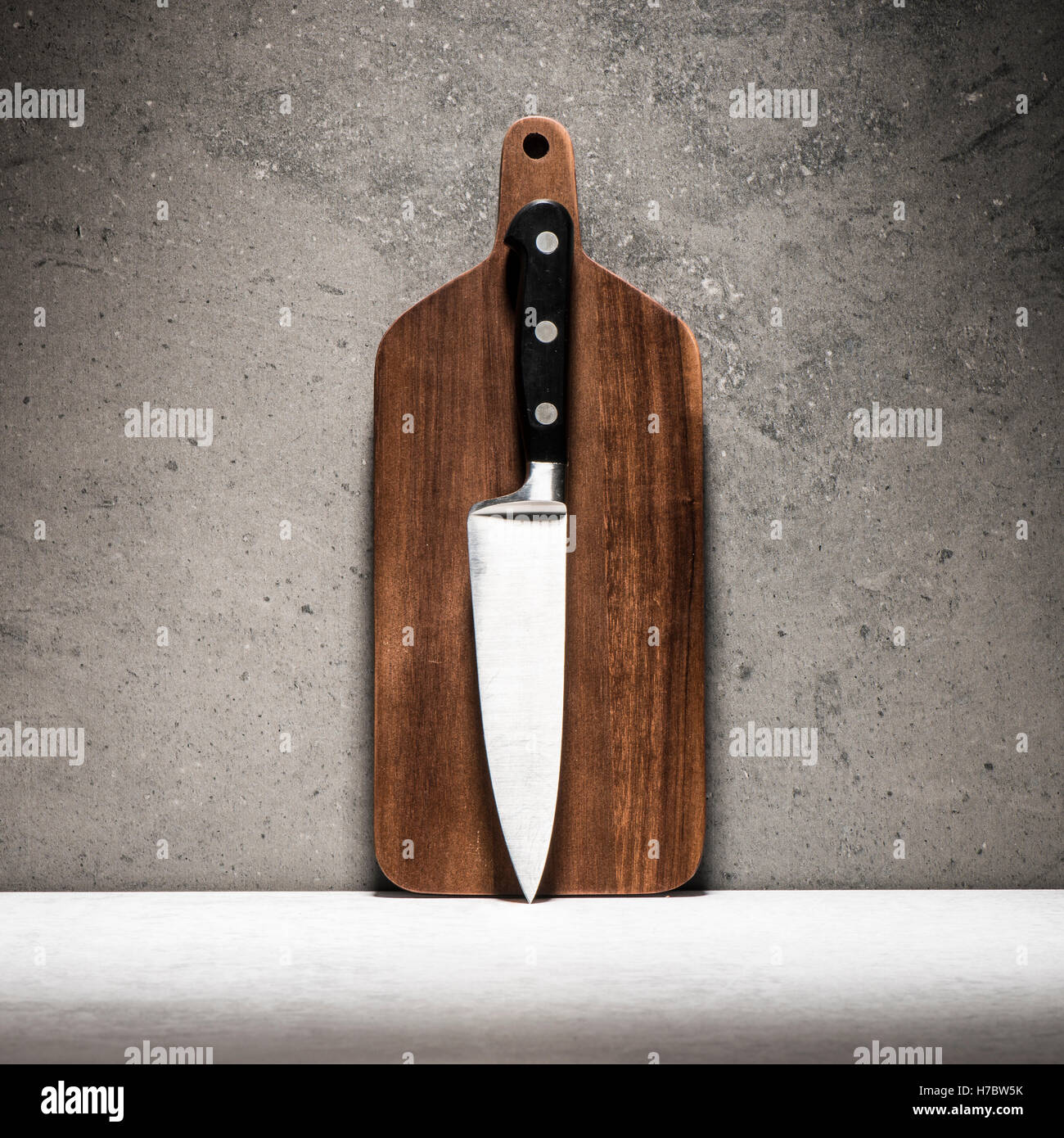 Kitchen knife and cutting board on stone table. Culinary theme still