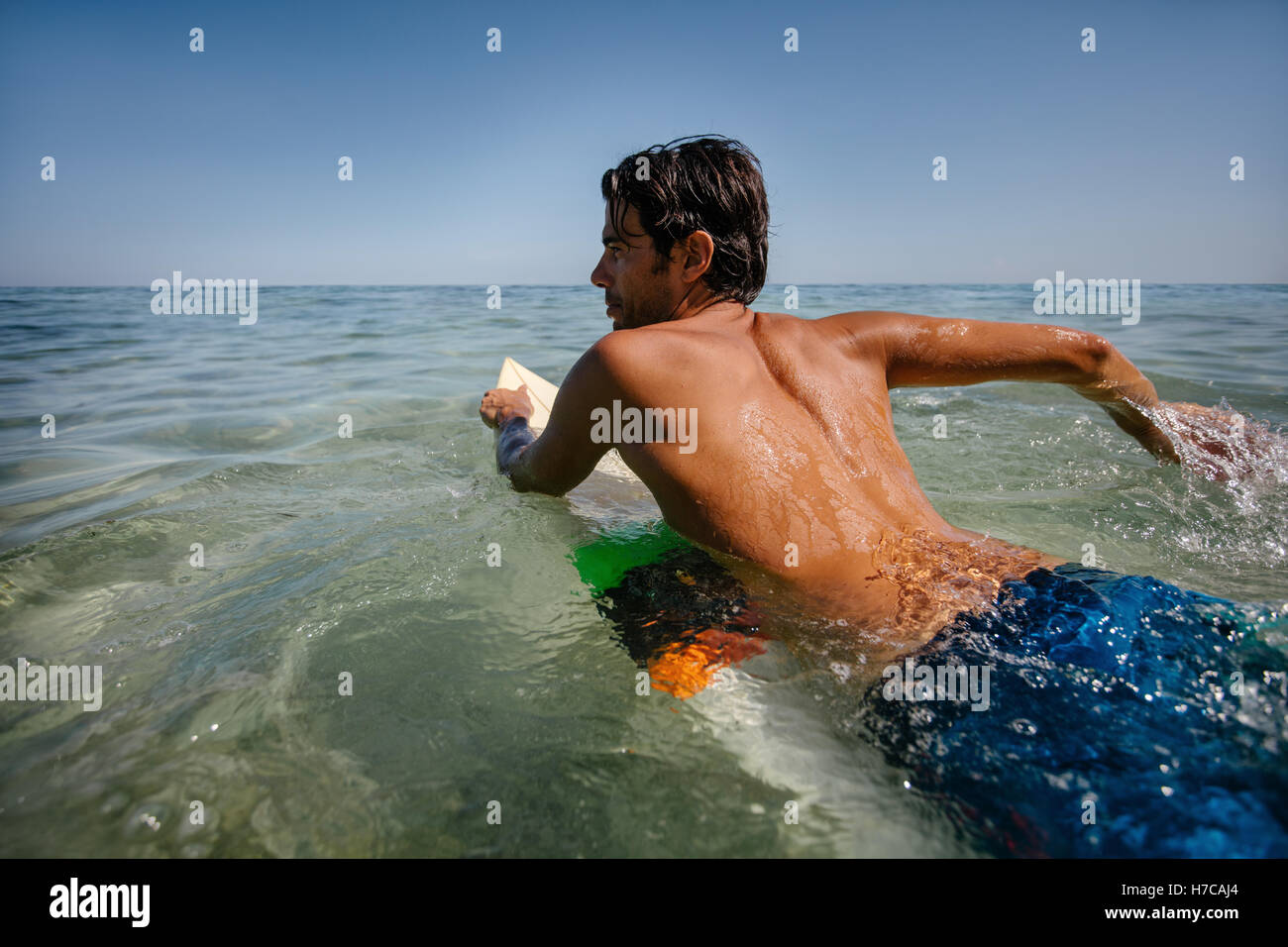 Shot of young man drifting on surfboard in the ocean. Young man enjoying a surf in sea water. Stock Photo