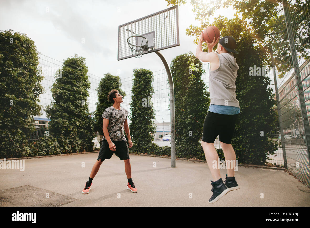 Young man taking jump shot with friend on basketball court. Streetball players having fun on court. Two teenage friends playing Stock Photo