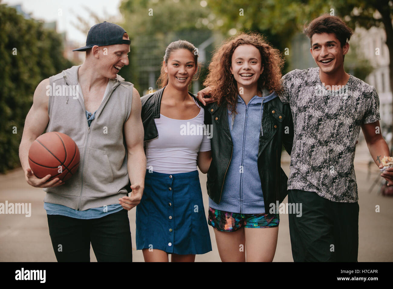 Portrait of four young friends walking together and smiling. Mixed race group of people enjoying a walk outdoors. Stock Photo