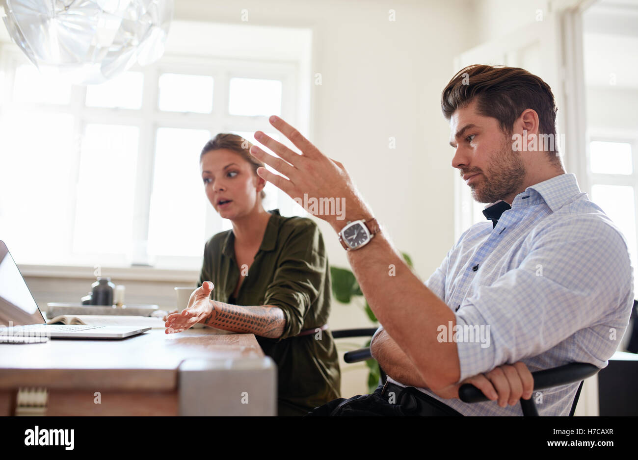 Shot of young couple sitting together at table with laptop and discussing work. Young man and woman working at home office. Stock Photo