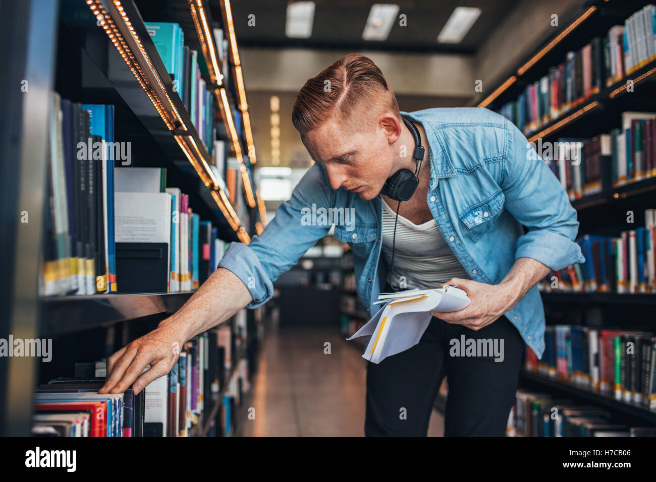 Shot of young man looking for a book in shelf. university student in library selecting a book. Stock Photo