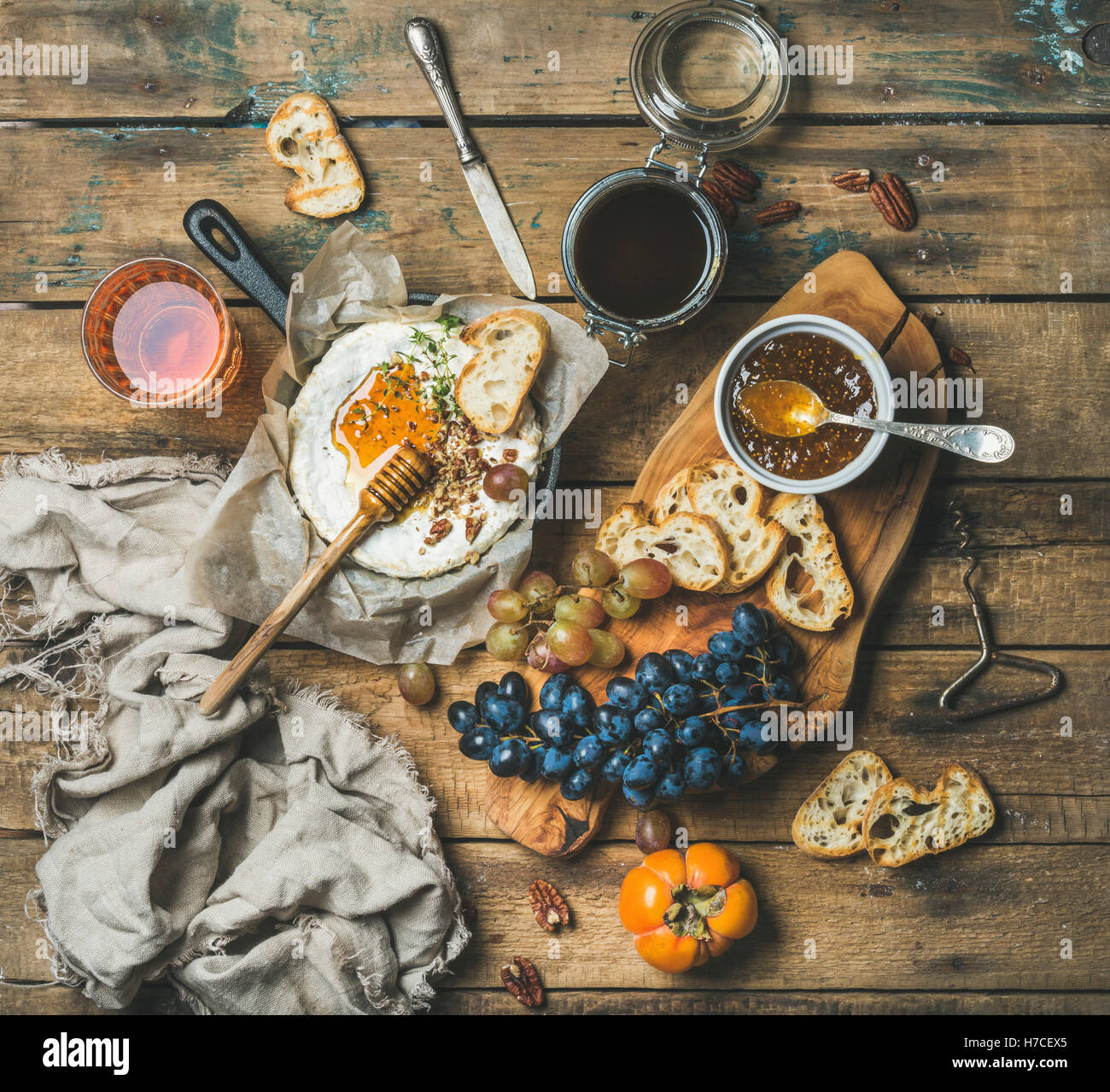 Cheese, fruit and wine set. Camembert in small pan, honey, fig jam, persimmon, grapes, pecan nuts, grilled baguette slices and g Stock Photo