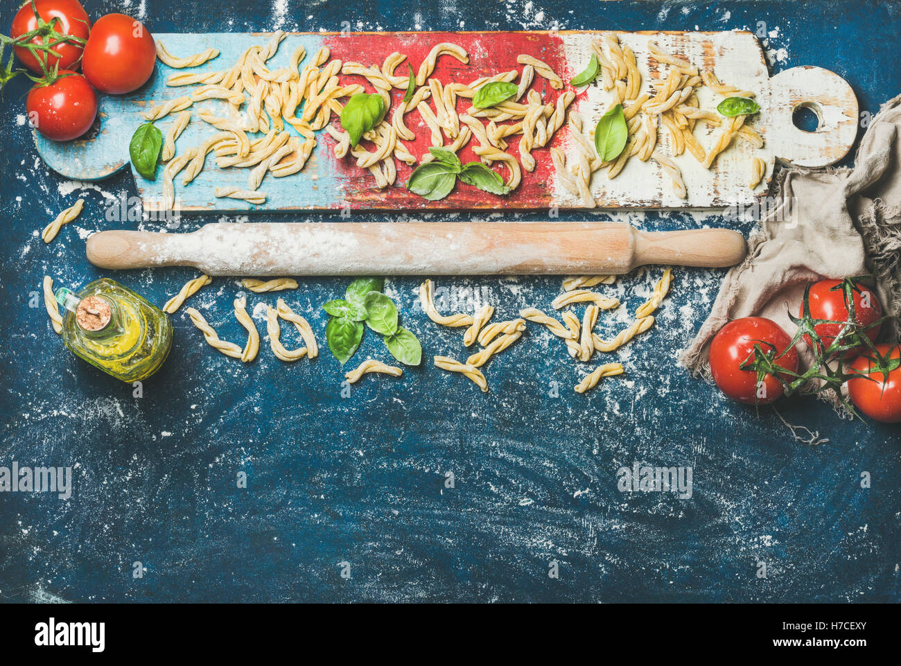 Ingredients for cooking Italian dinner. Fresh pasta casarecce, tomatoes, basil leaves and bottle of olive oil on colorful painte Stock Photo