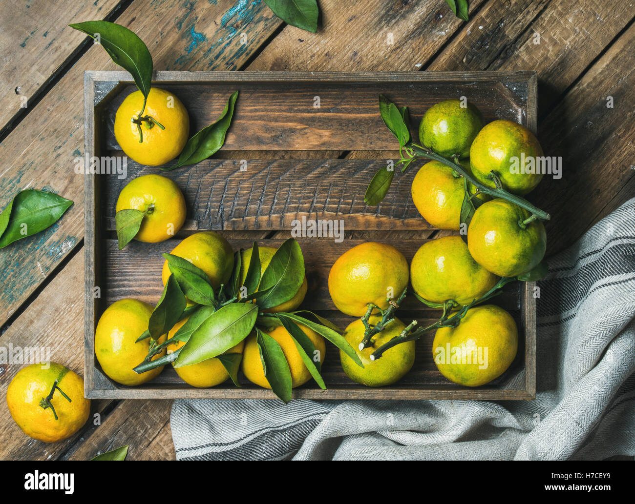 Fresh green and orange Mediterranean tangerines with leaves in wooden box over rustic wooden background, top view, copy space, h Stock Photo