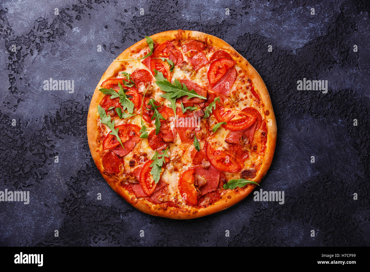 Pizza with ham, tomato and arugula leaves on dark background Stock Photo